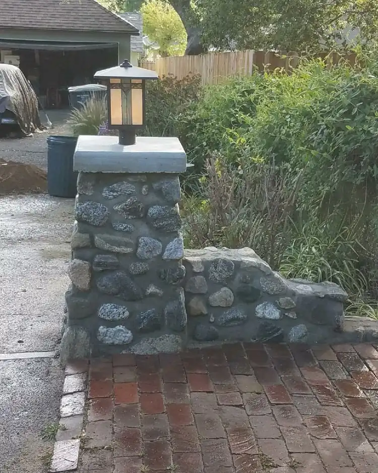 A river rock column with a concrete cap and a lantern, beside a used brick walk