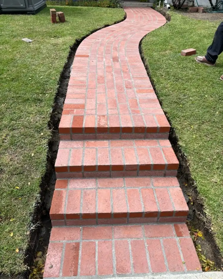 A red brick walk curving across a green lawn with three brick steps