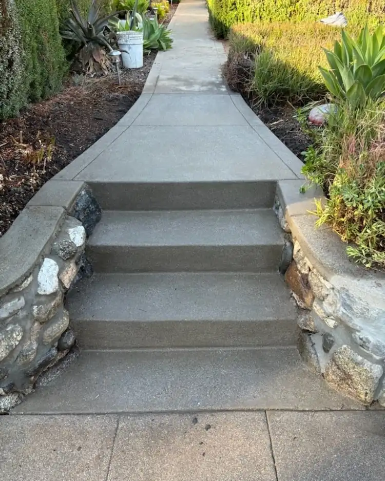 Broad concrete steps rising between low stone walls and planting