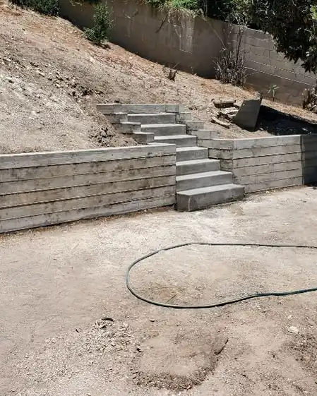 A finished poured concrete retaining wall and steps on a slope