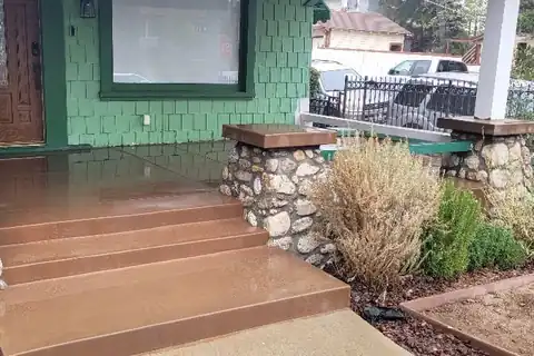 New stained concrete porch steps between river rock piers on a green Craftsman house