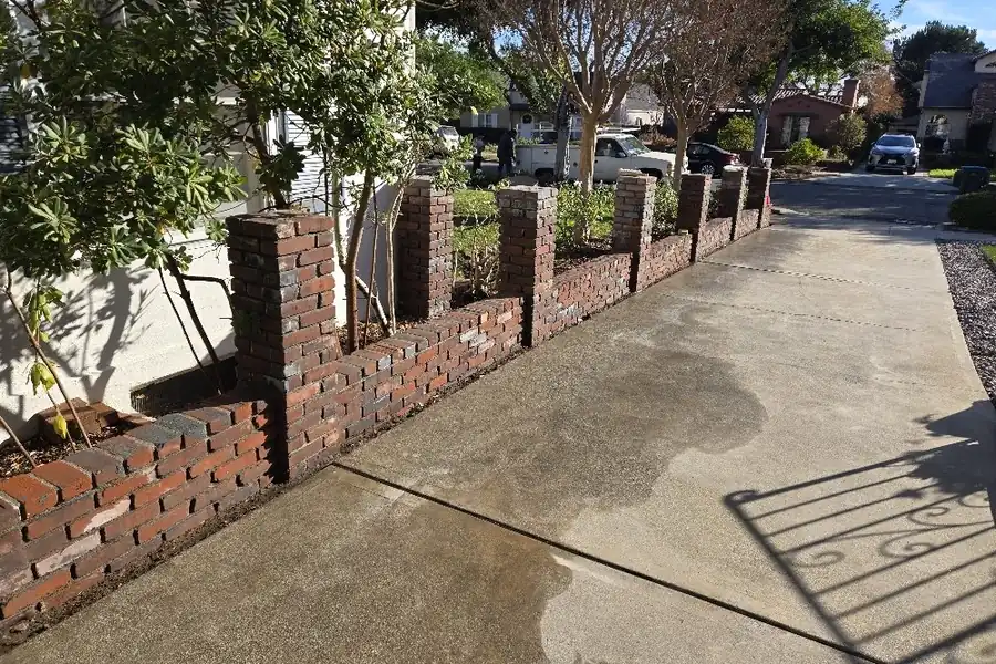 Brick pilasters and a low brick wall along a freshly poured sidewalk